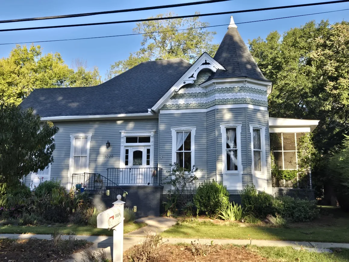 Blue-gray historic home with decorative shingles, turret, white trim, and a steep roofline